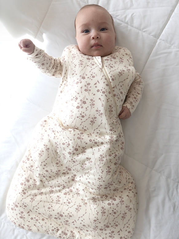 Baby in a floral sleep bag lying on a white surface