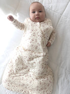 Baby in a floral sleep bag lying on a white surface