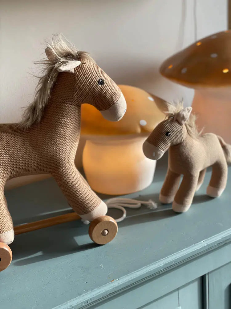 Two plush toy horses on a surface with a lamp in the background