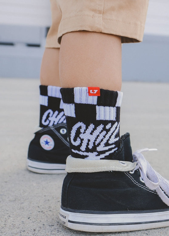 Black high-top sneakers with white laces and socks featuring a black and white checkerboard pattern.