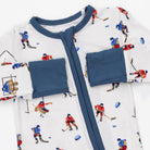 White baby romper with a navy blue collar, zipper, and pocket trim, featuring an all-over print of children playing hockey.