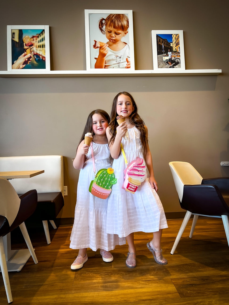 Two young girls in a restaurant setting with ice cream cones and bags.