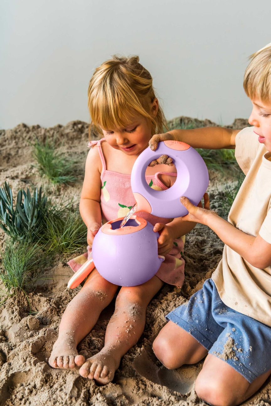 Two children playing with purple sand toys on a sandy beach.