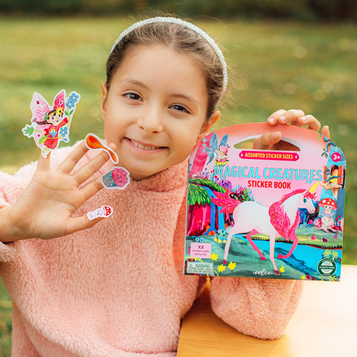Girl holding a 'Magical Creatures' sticker book and stickers outdoors