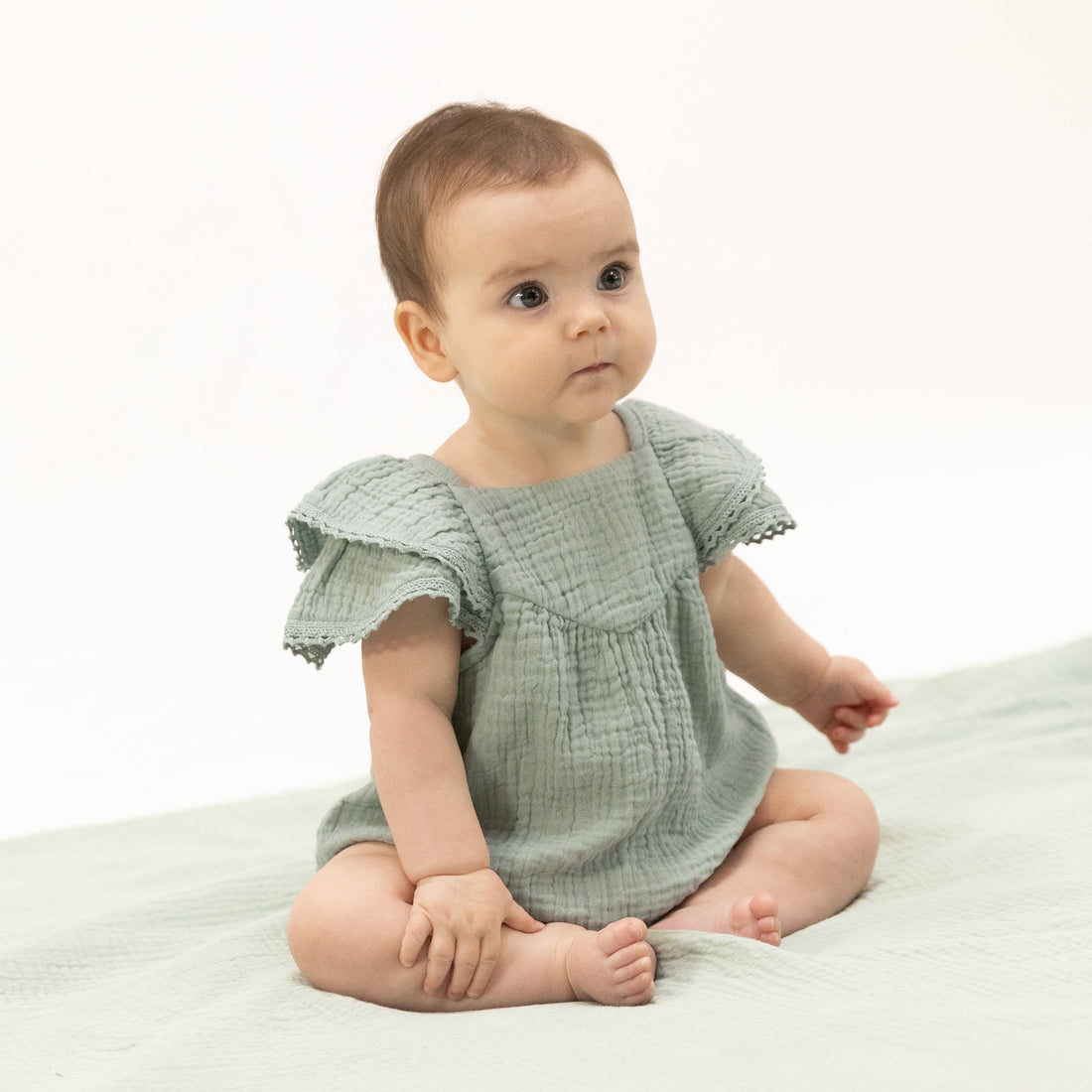 Baby wearing a light green dress sitting on a white surface