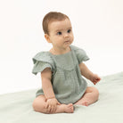 Baby wearing a light green dress sitting on a white surface