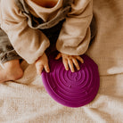 Child's hands holding a purple lid on a beige blanket
