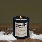 Candle with 'Stag & Fin Candle Co' label on a wooden surface with snow-like material