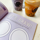 Book with drawing instructions next to bubble tea drinks.