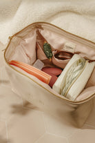 Beige makeup bag with cosmetic items on a beige surface