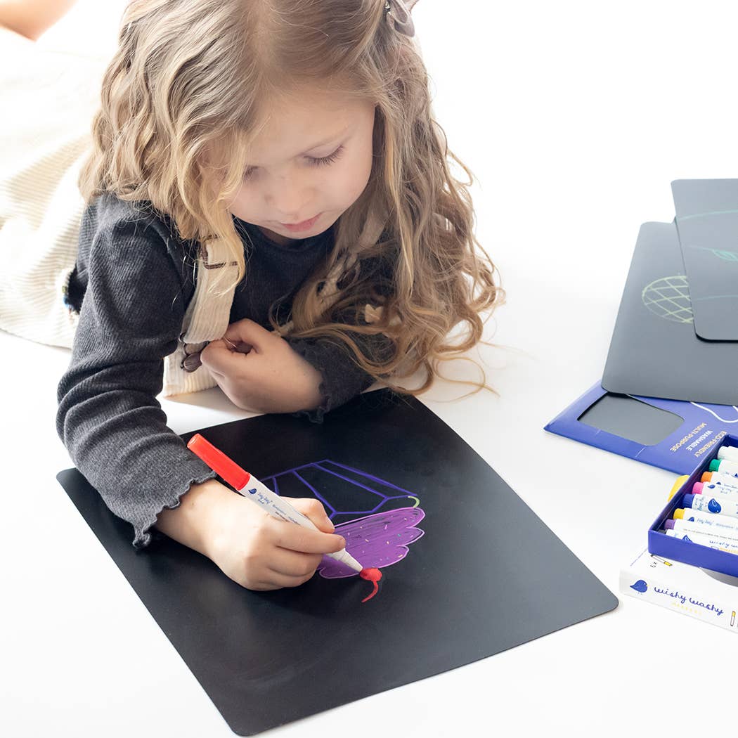 Child drawing on a black mat with art supplies around