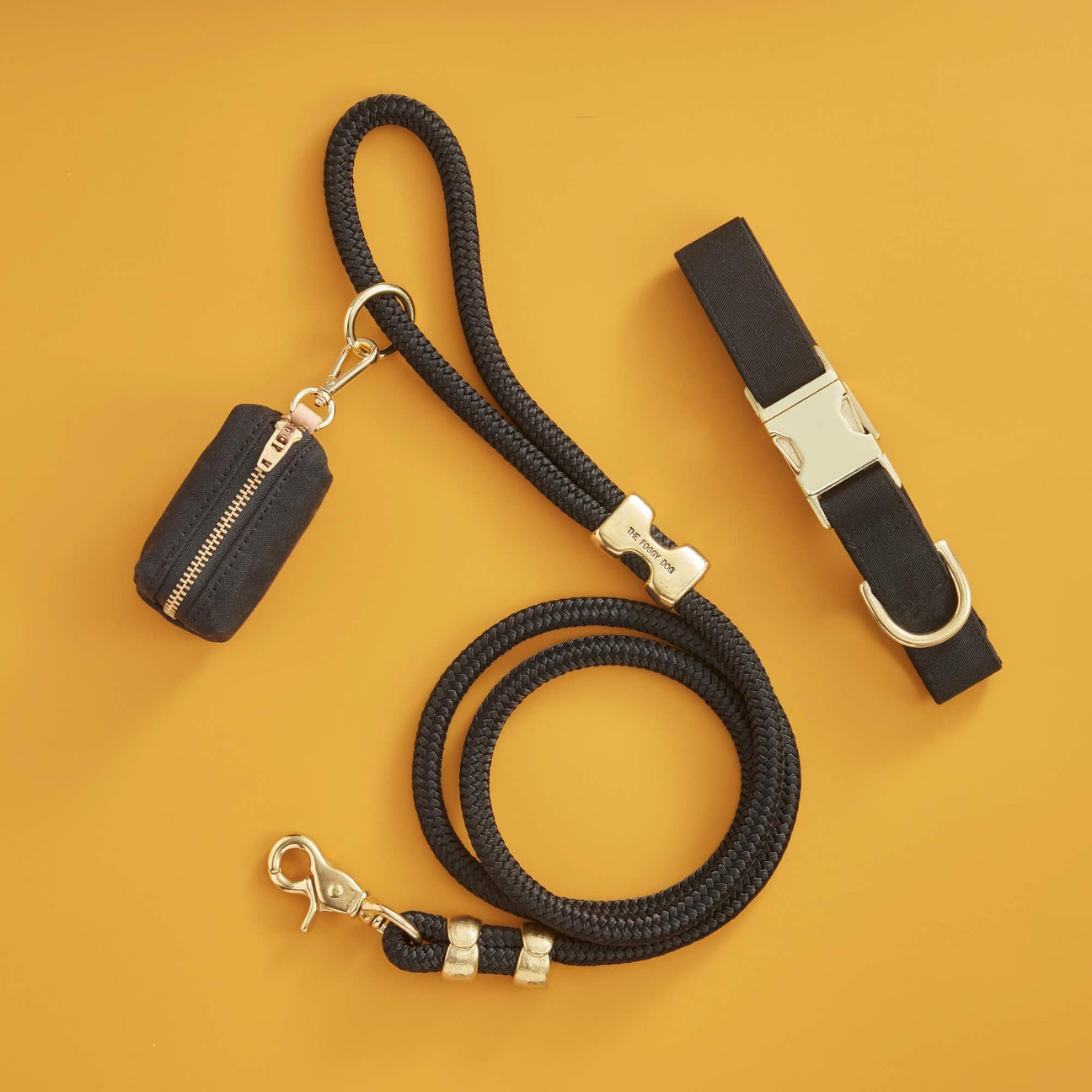 Black dog leash with gold hardware and a black pouch on a mustard yellow background