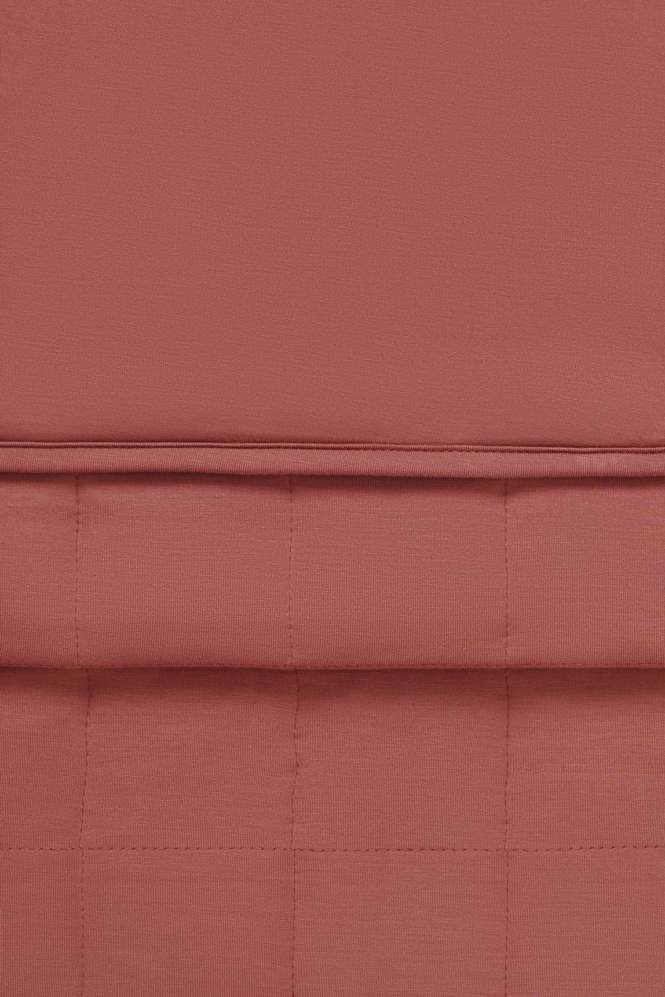 A close-up of a warm colored fabric napkin with a quilted grid pattern and a horizontal stitched seam.