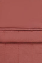 A close-up of a warm colored fabric napkin with a quilted grid pattern and a horizontal stitched seam.