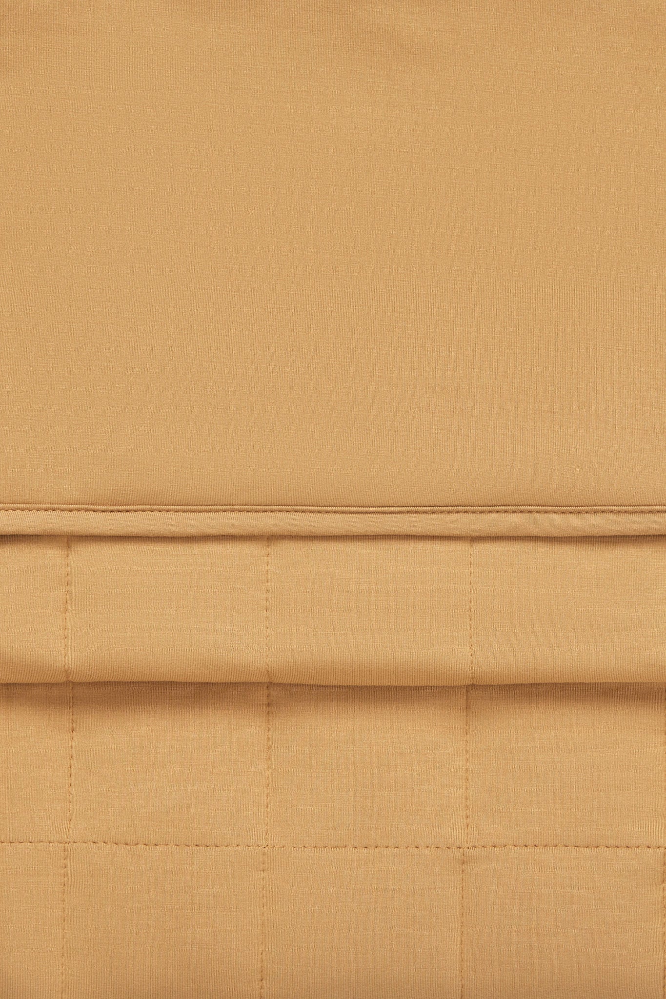 A close-up of a warm tan or camel-colored fabric with a quilted grid pattern and a horizontal stitched seam.