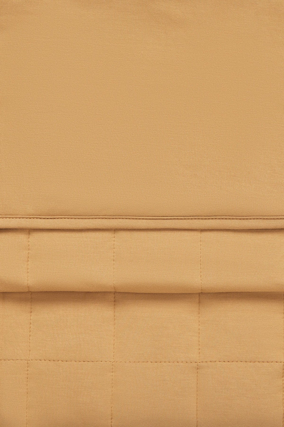 A close-up of a warm tan or camel-colored fabric with a quilted grid pattern and a horizontal stitched seam.