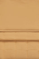 A close-up of a warm tan or camel-colored fabric with a quilted grid pattern and a horizontal stitched seam.