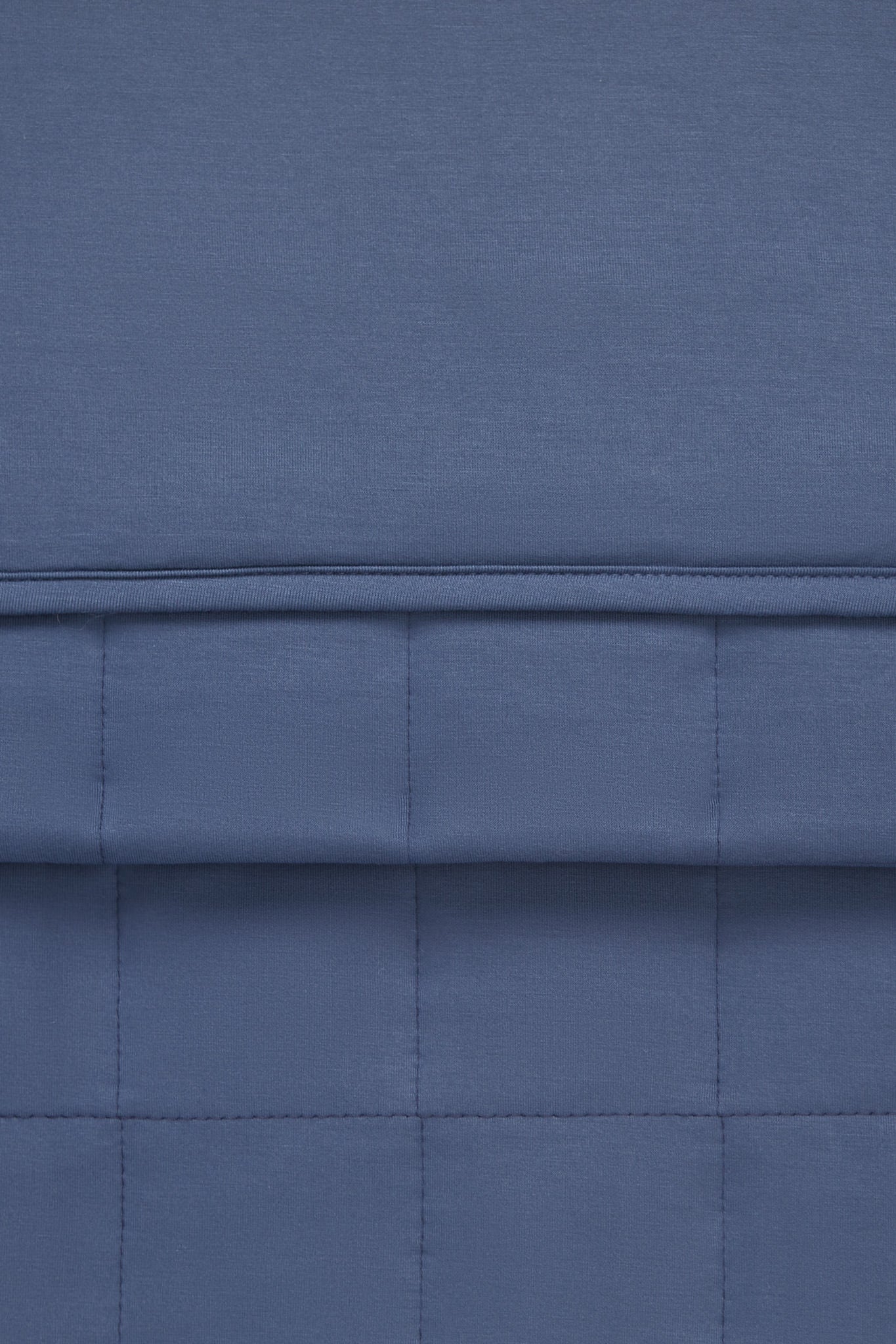 A close-up of a blue quilted fabric with stitched paneling and a horizontal seam.