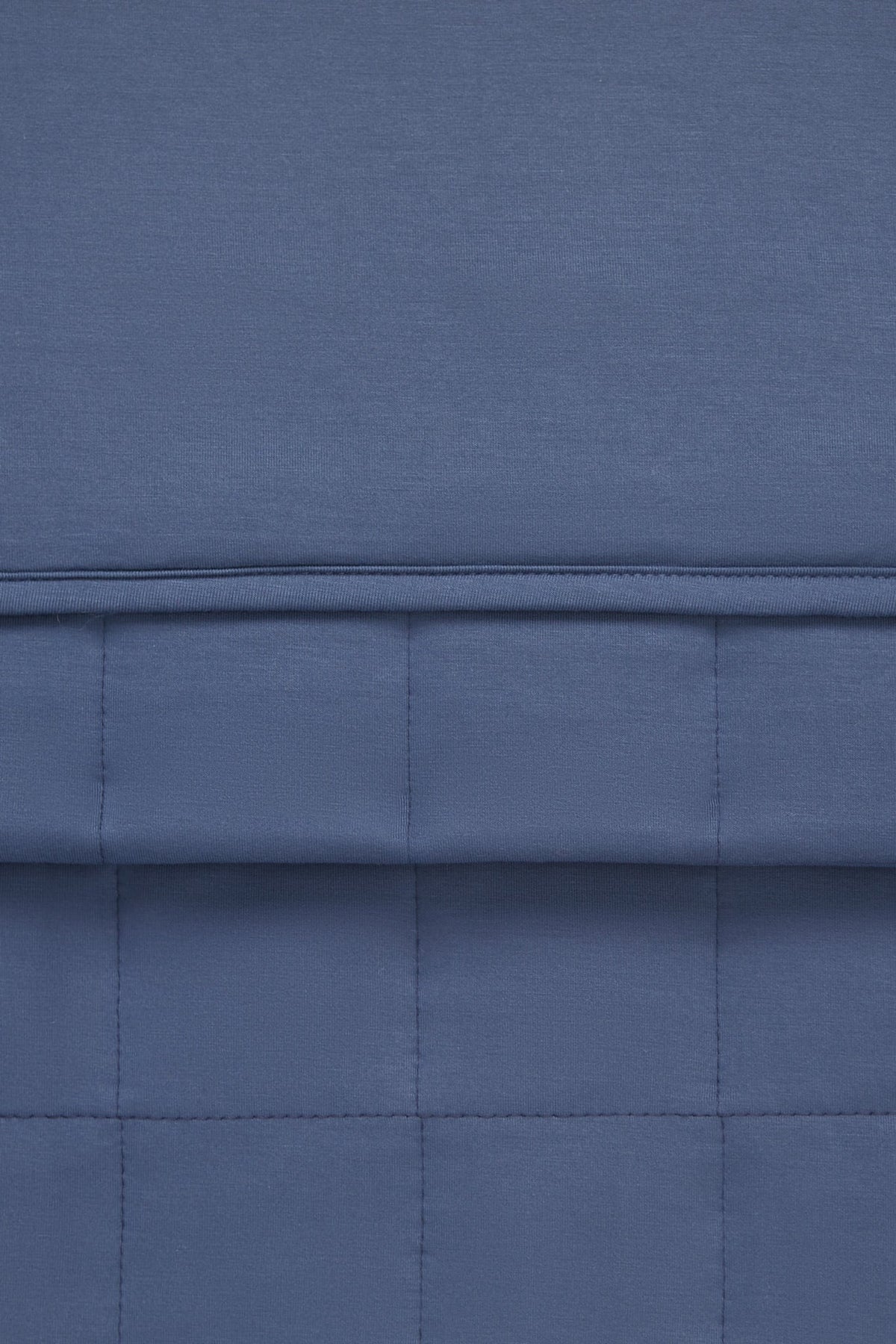 A close-up of a blue quilted fabric with stitched paneling and a horizontal seam.