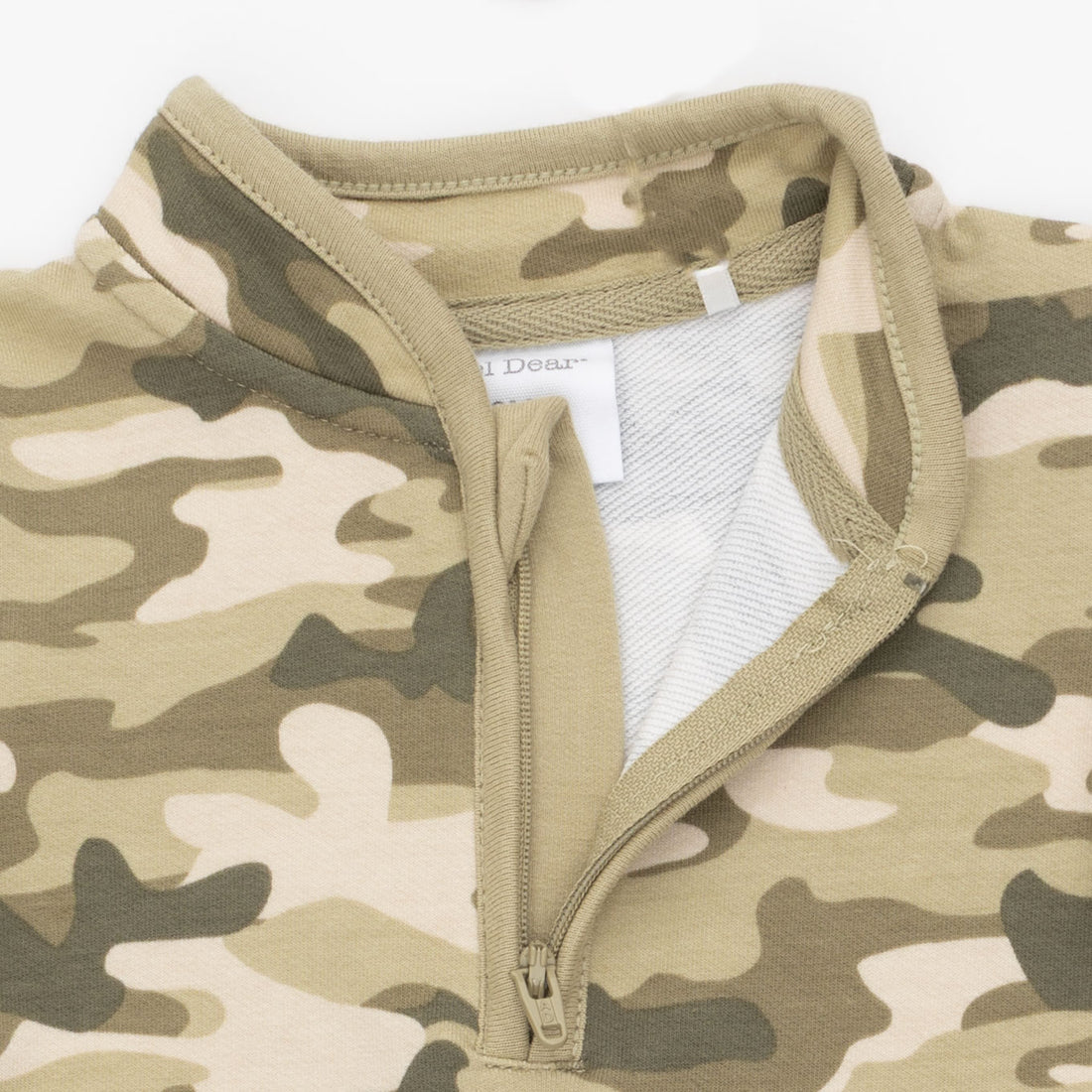 Close-up of a camouflage quarter-zip garment with a tan collar and zipper, showing a white inner lining and a partially visible 'Dear' brand label.