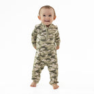 A smiling baby standing on a white background, wearing a long-sleeve camouflage one-piece jumpsuit with a half-zip neckline.