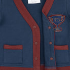 Close-up of a navy blue cardigan sweater with rust red trim, button closure, and a blue and red embroidered trophy patch on the chest.