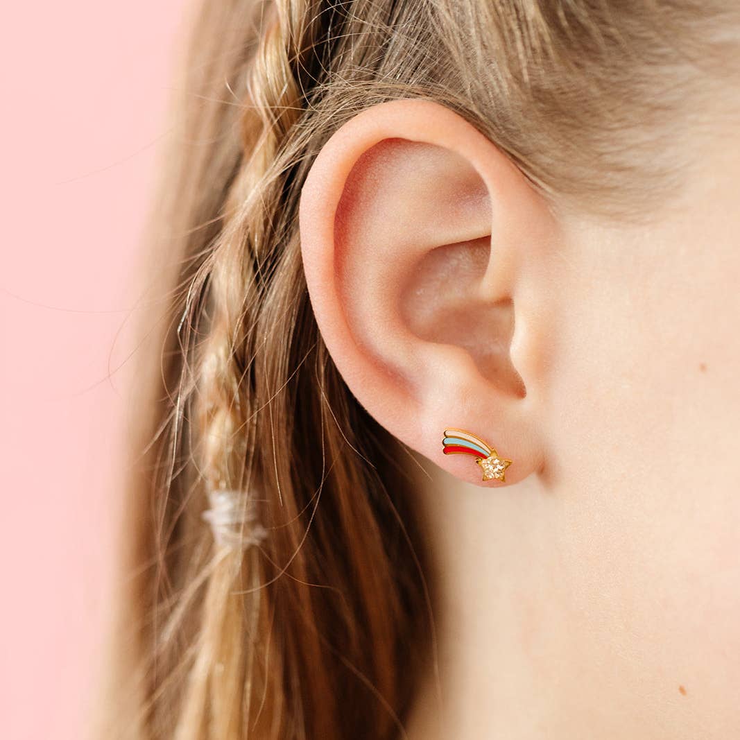 Close-up of an ear wearing a gold earring with a red, white, and blue design against a pink background