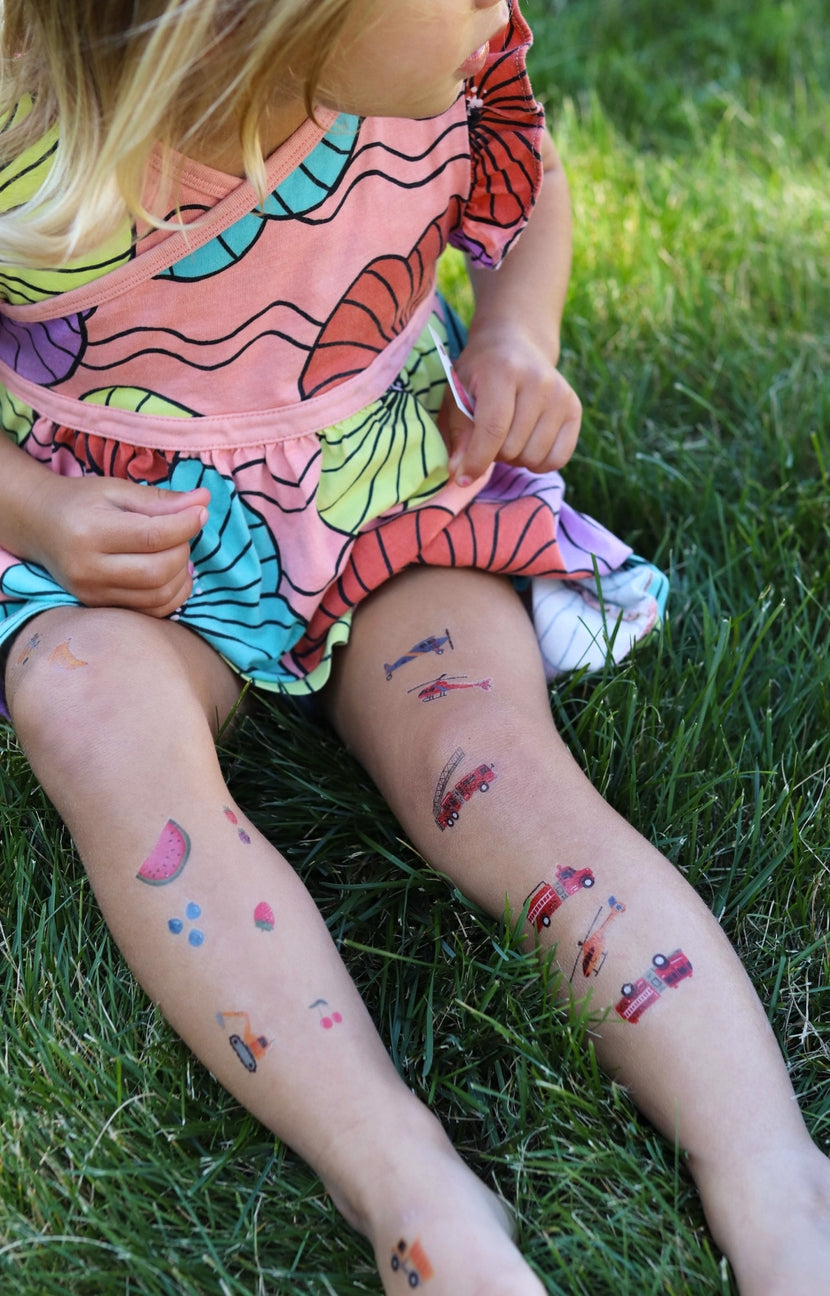 Child with colorful temporary tattoos on legs sitting on grass