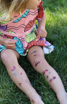 Child with colorful temporary tattoos on legs sitting on grass