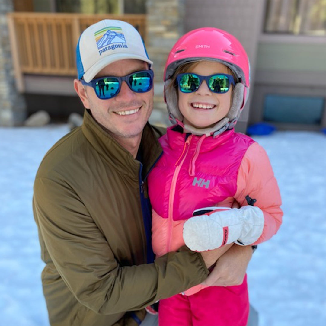 Man and young girl in winter gear posing for a photo outdoors.