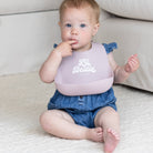 Baby wearing a bib with 'Lil' Bestie' text, sitting on a couch.