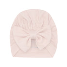 A pale pink baby turban hat with a large bow on the front, shown flat against a white background.