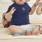 Baby wearing a navy blue shirt and white shorts with a pattern, sitting on a beige surface.