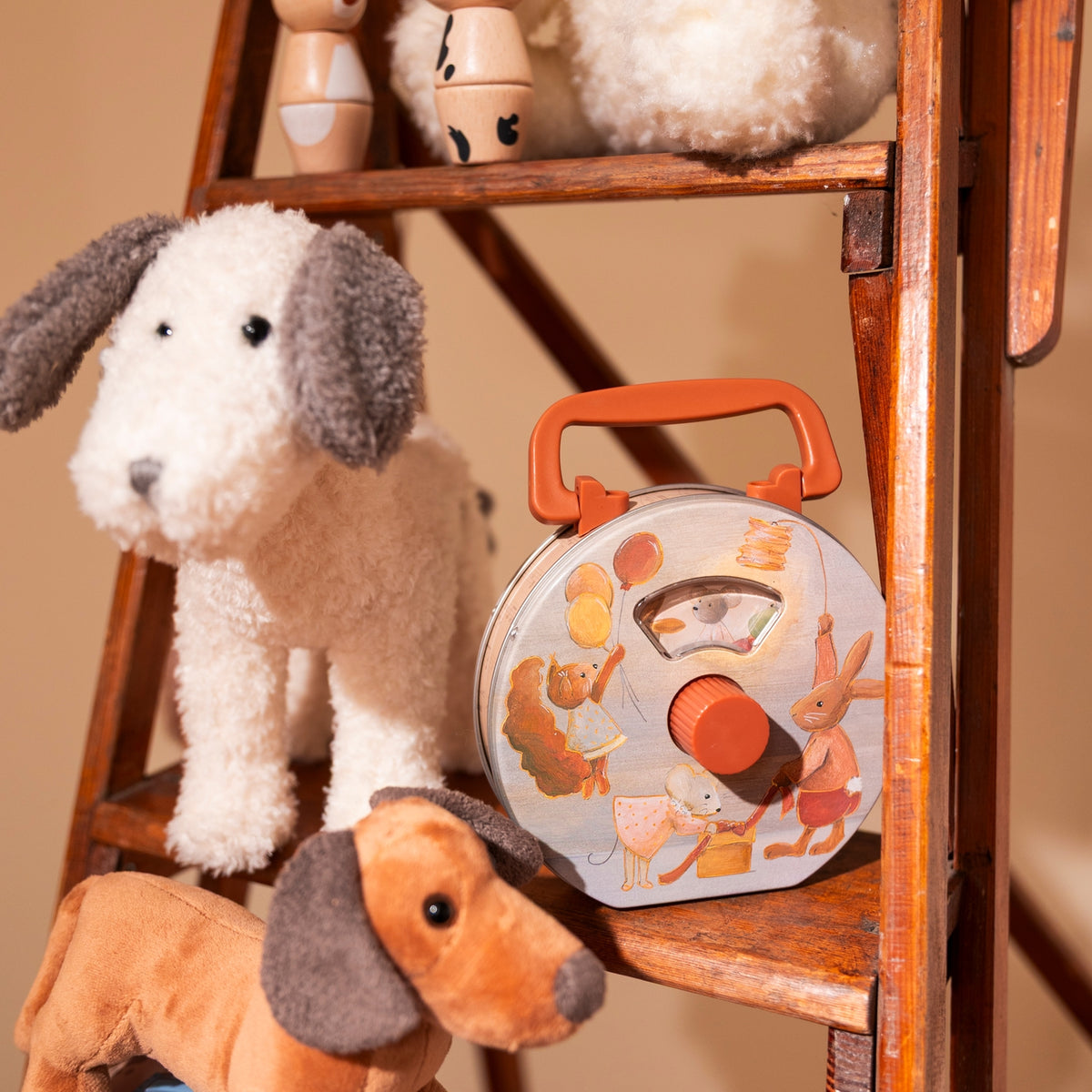Stuffed dog toys with a round toy box on a wooden shelf against a beige wall.
