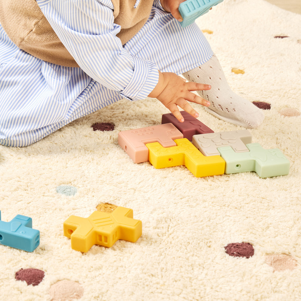 Child playing with colorful puzzle pieces on a sandy surface