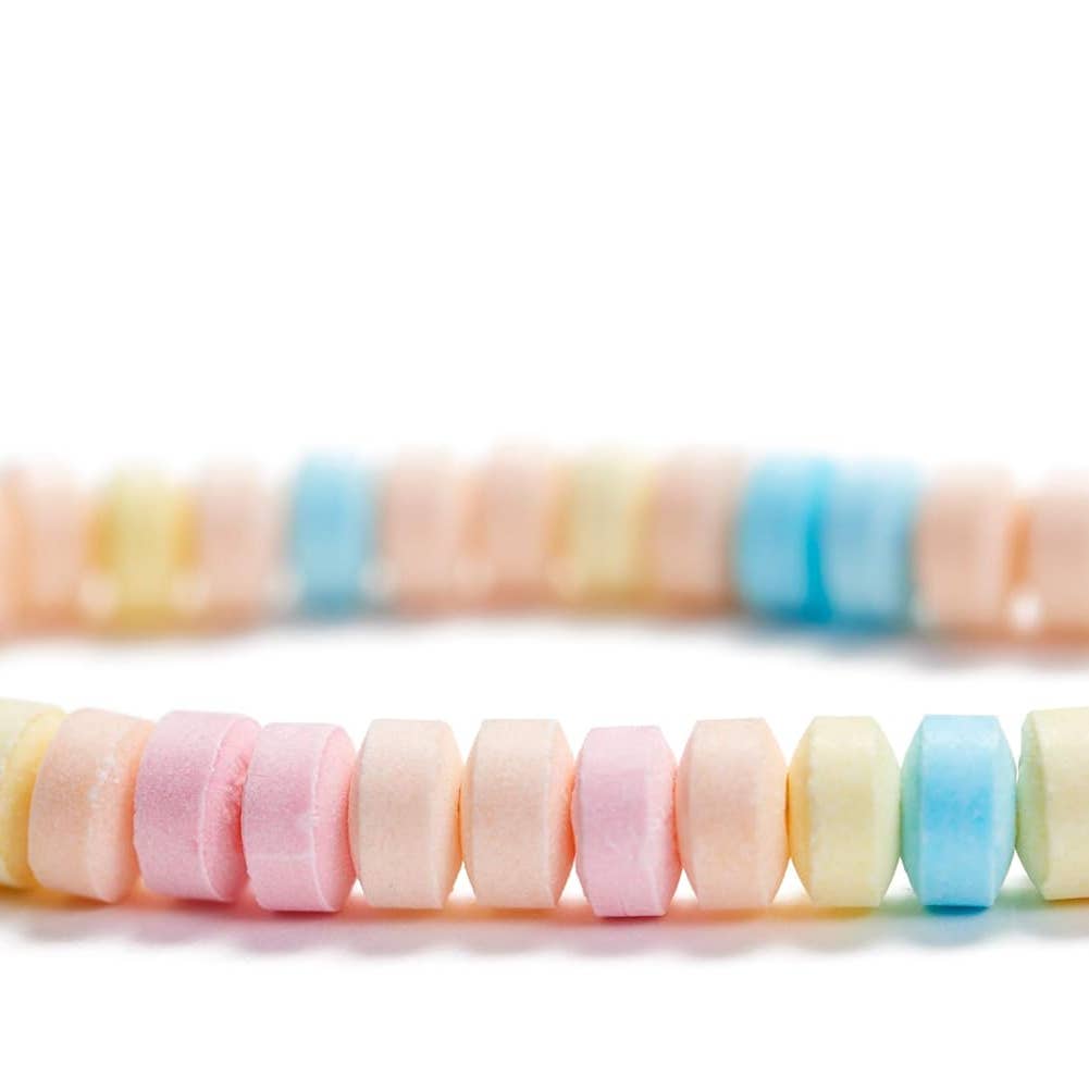 A close-up of pastel candy-coated beads or beads arranged in two rows on a white background, showing soft pink, peach, pale yellow, and light blue colors.