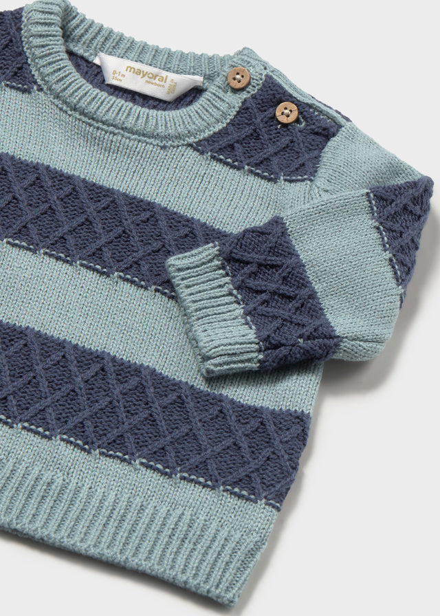 A close-up of a baby knit sweater with horizontal stripes in light sage green and navy blue, featuring textured diamond-knit patterns, a crew neck, and two wooden buttons on the shoulder.