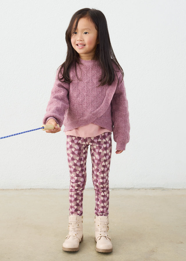 Young girl wearing a pink sweater and patterned leggings holding a blue toy.