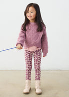 Young girl wearing a pink sweater and patterned leggings holding a blue toy.