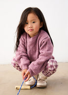Child wearing a pink sweater and patterned pants, holding a jump rope on a light background