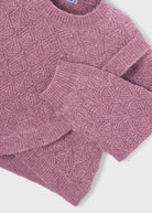 A close-up of a dusty rose pink cable-knit sweater, showing the detailed knit pattern and ribbed collar, cuffs, and hem against a white background.