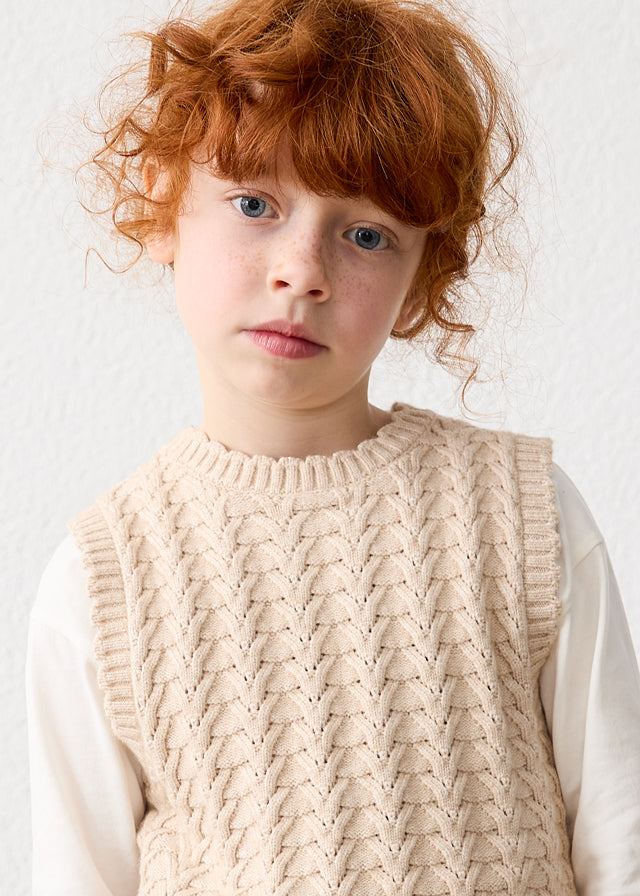 Child wearing a beige knitted vest against a plain background
