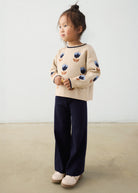 Child wearing a beige sweater with floral patterns and dark pants on a plain background