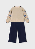 Beige sweater with floral patterns and navy pants on a light gray background