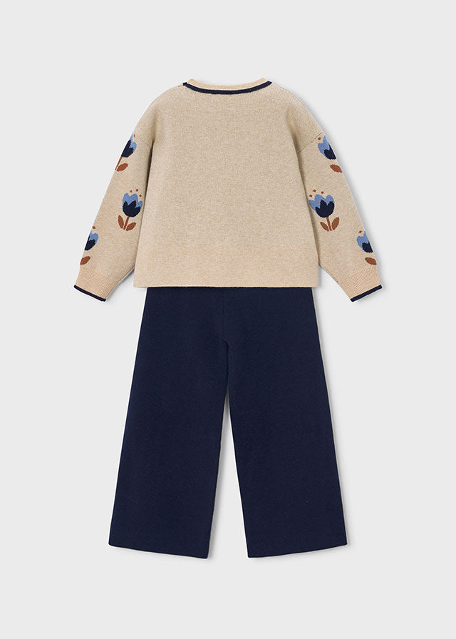 Beige sweater with floral patterns and navy pants on a light gray background