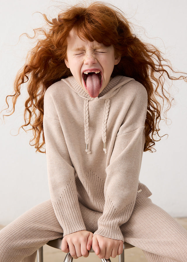 Child in a beige sweater and pants sitting on a chair with a white background