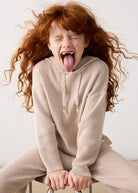 Child in a beige sweater and pants sitting on a chair with a white background