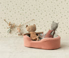 Two stuffed animals in a pink bed with a decorative wall and clothesline in the background.