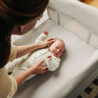 A beige UPPAbaby Remi V2 Playard shown with an attached changing station and bassinet insert, with an adult standing next to it.