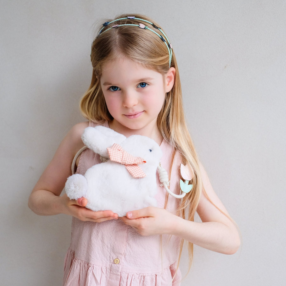Young girl holding a white teddy bear with a pink bow against a plain background